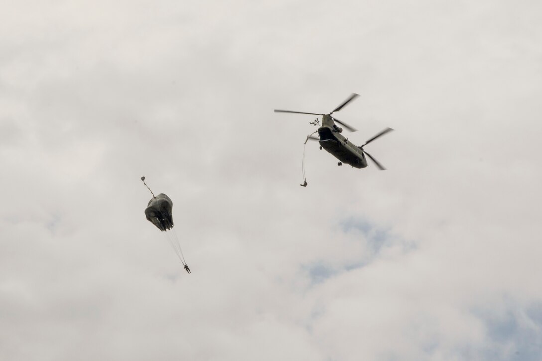 Soldiers jump from a helicopter with parachutes.