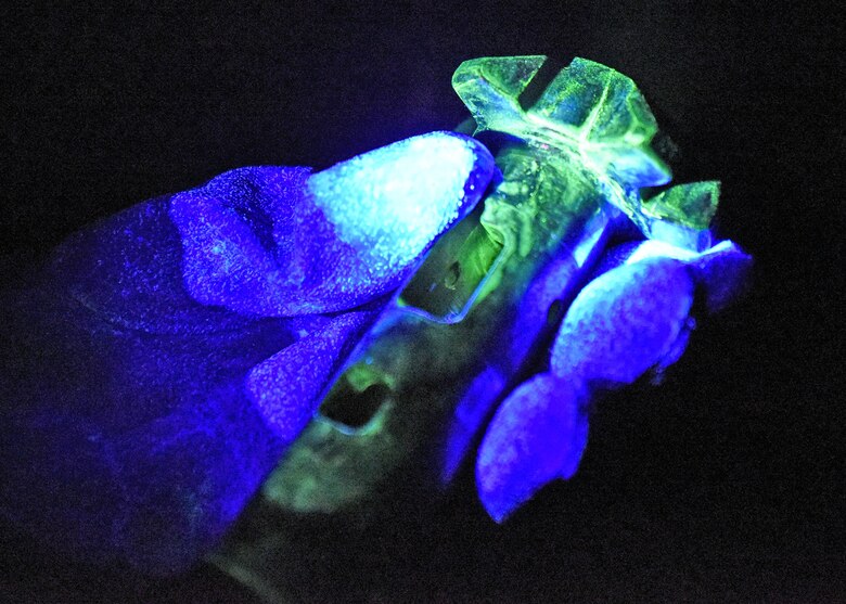 Photo of an aircraft part with fluorescent penetrant glowing green under black light.