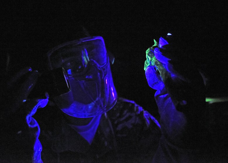 Photo of a U.S. Air Force Airman shining a UV light at an aircraft part in a dark room.