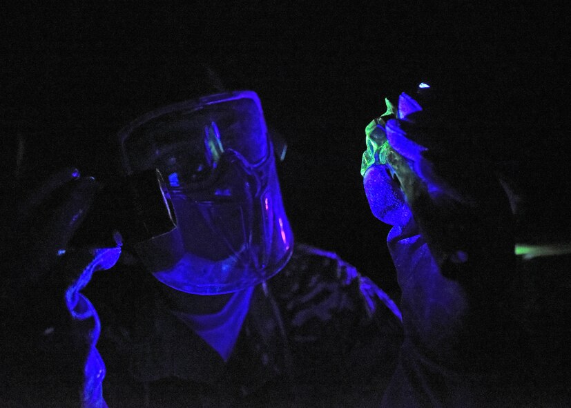 Photo of a U.S. Air Force Airman shining a UV light at an aircraft part in a dark room.