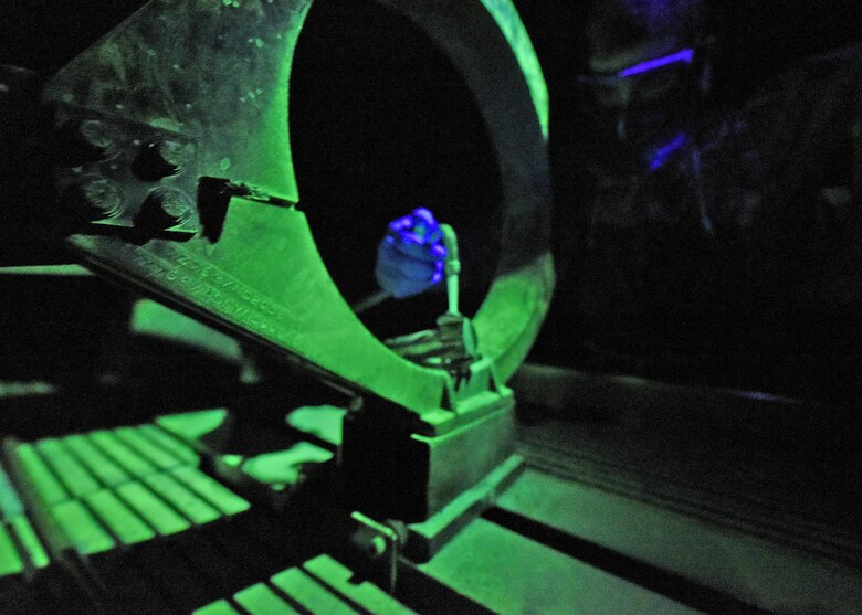 Photo of a U.S. Air Force Airman pouting fluorescent penetrant on an aircraft part.