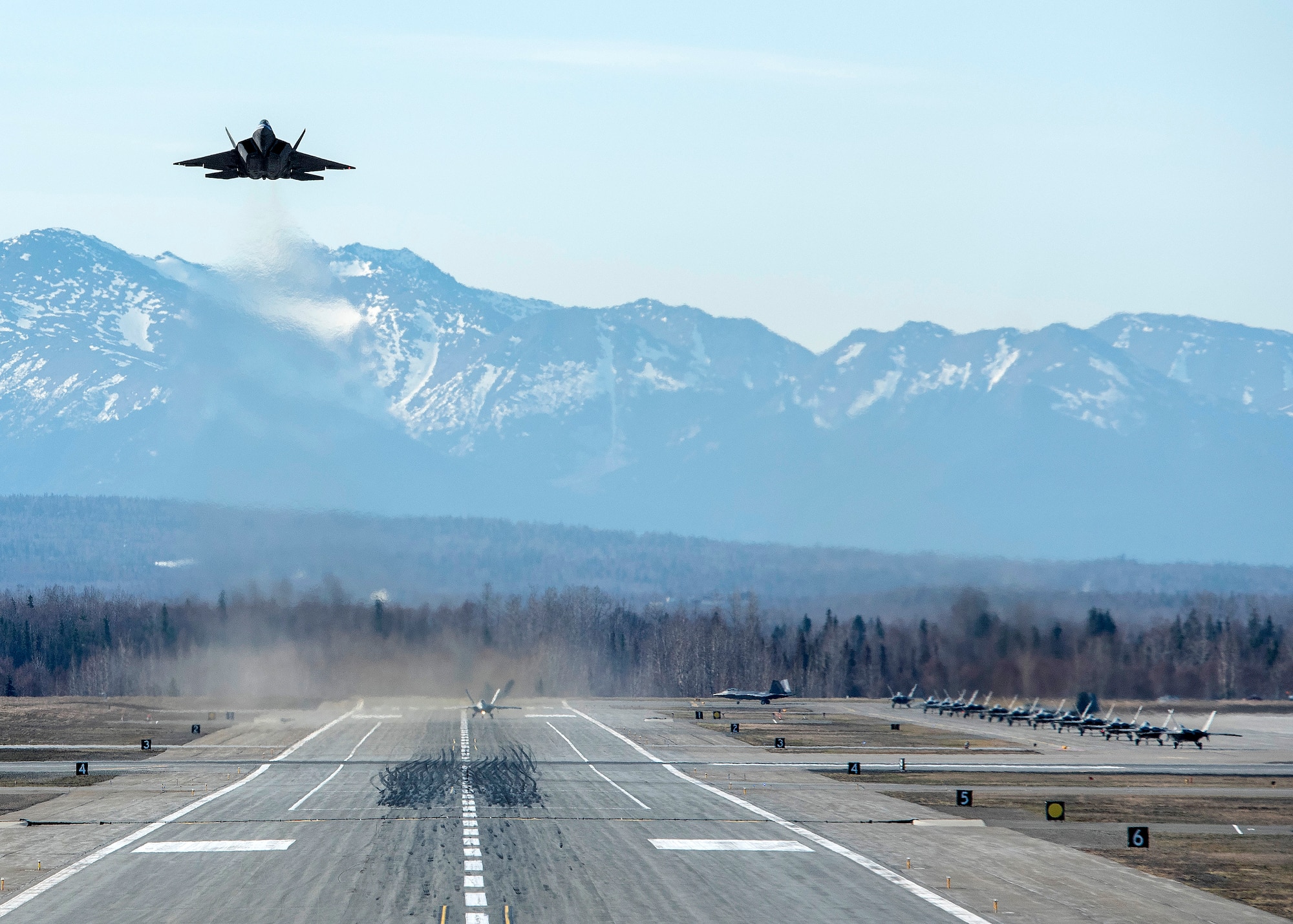 A U.S. Air Force F-22 Raptor takes off while other Raptors taxi to the runway following a close formation taxi known as an elephant walk, at Joint Base Elmendorf-Richardson, Alaska, May 5, 2020. This event displayed the ability of the 3rd Wing, 176th Wing and the 477th Fighter Group to maintain constant readiness throughout COVID-19 by Total Force Integration between active-duty, Guard and Reserve units to continue defending the U.S. homeland and ensuring a free and open Indo-Pacific.
