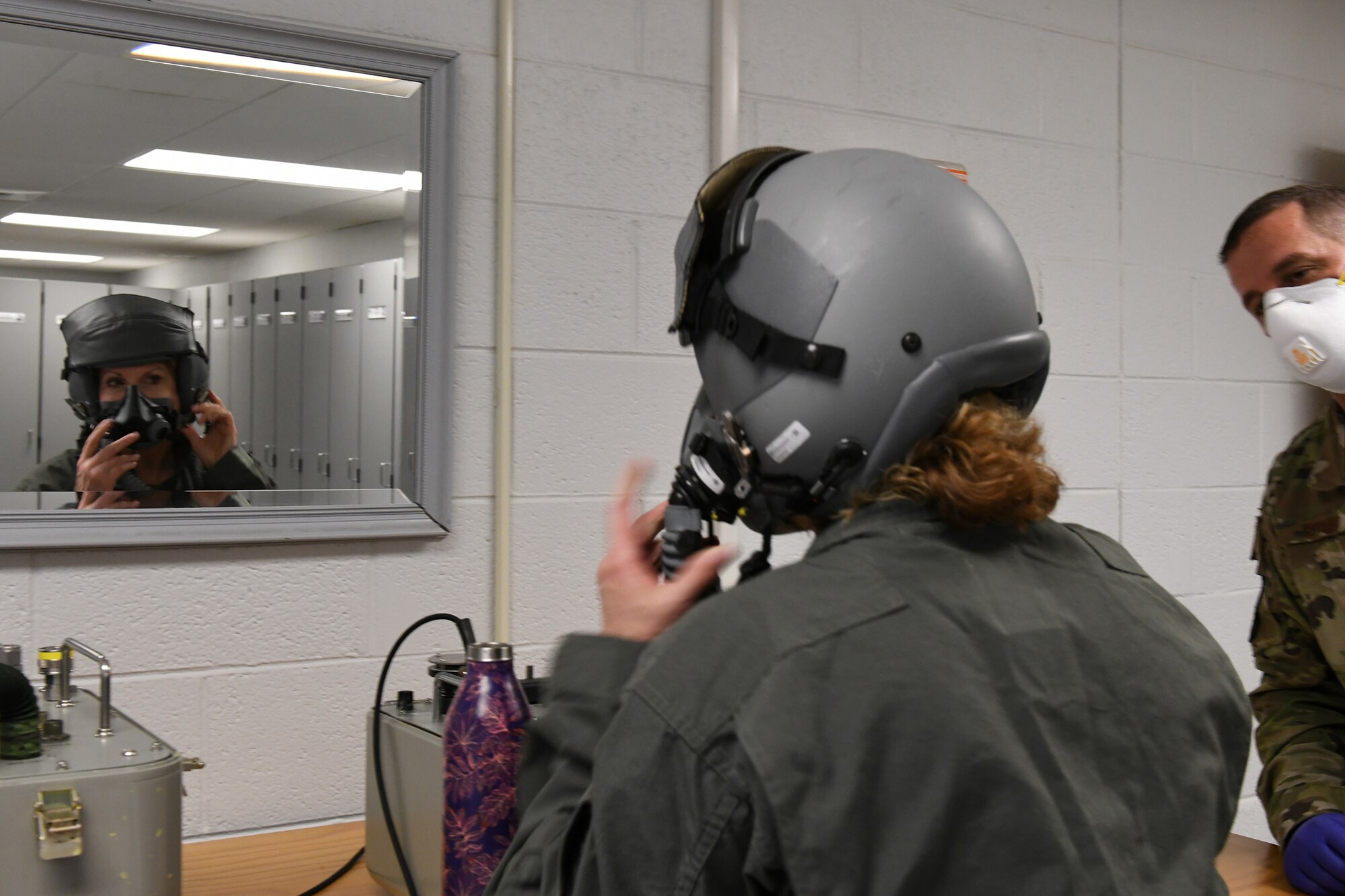 Photo shows Col. Farrell with her helmet on looking in the mirror as she fits her mask to her face.
