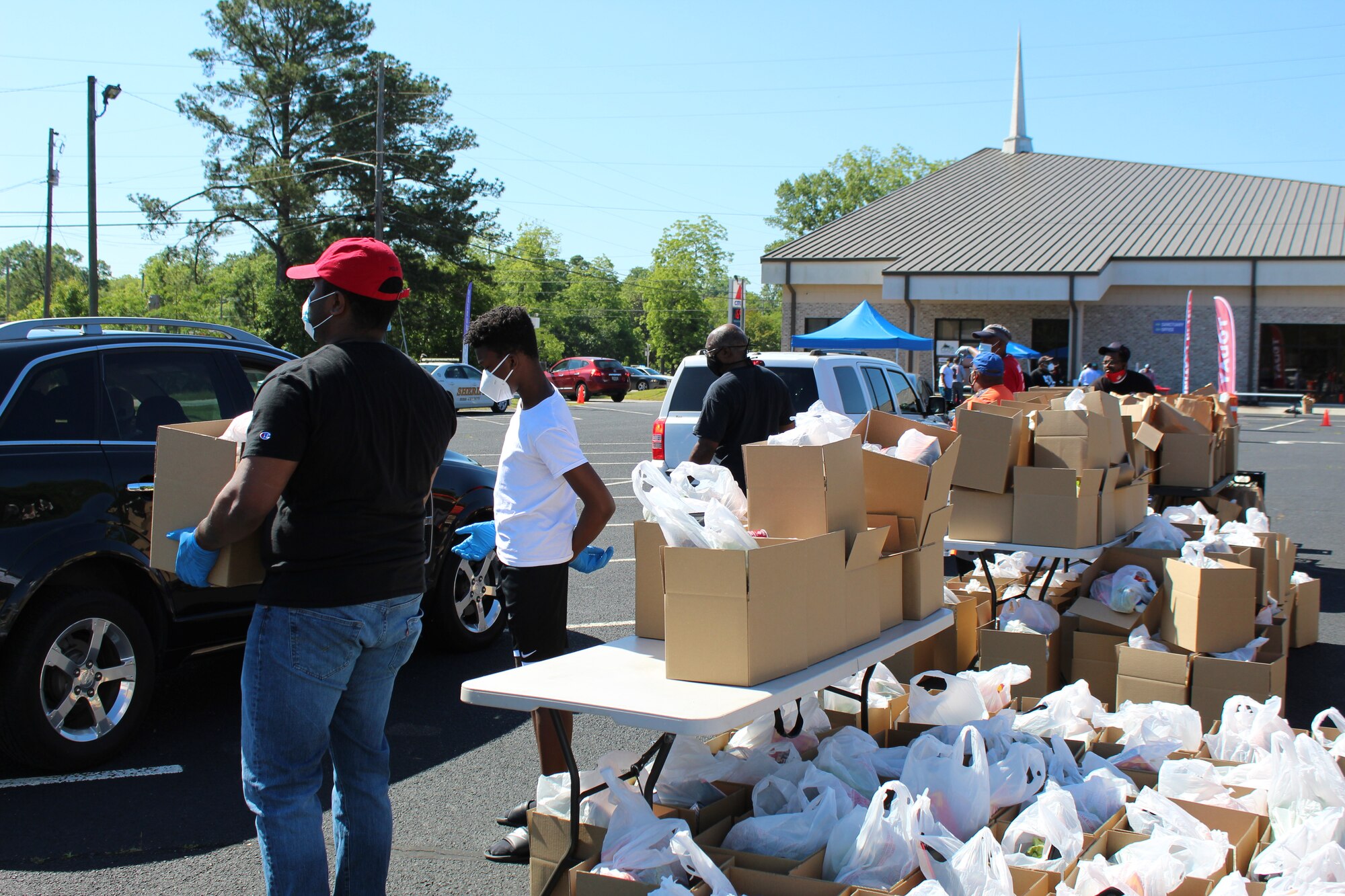 Photo shows individuals with boxes of food and handing them to families in cars as they drive by.