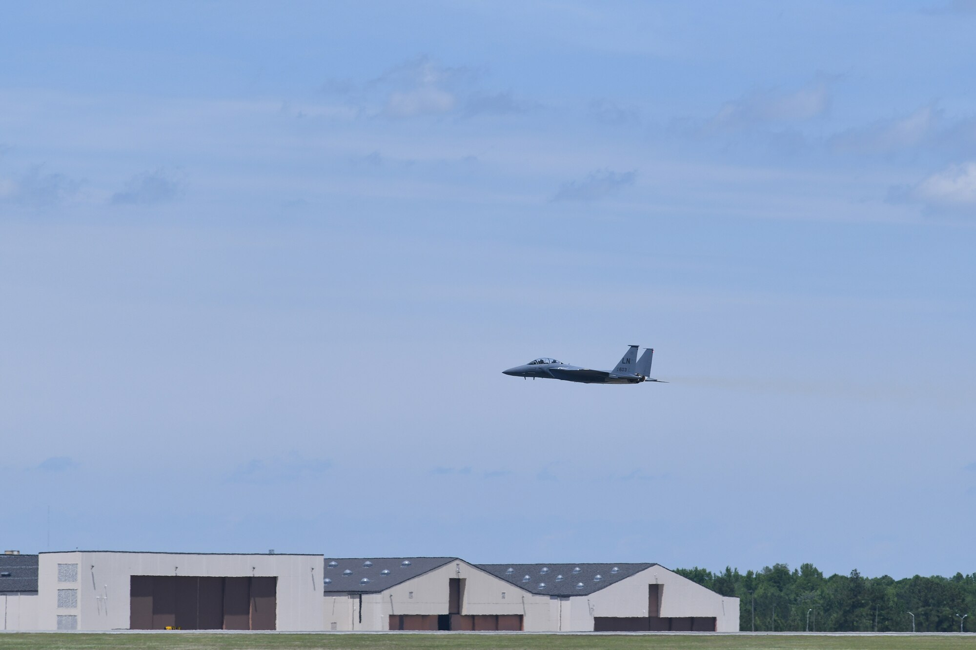 Photo shows an F-15 just above the tree line as it takes off.