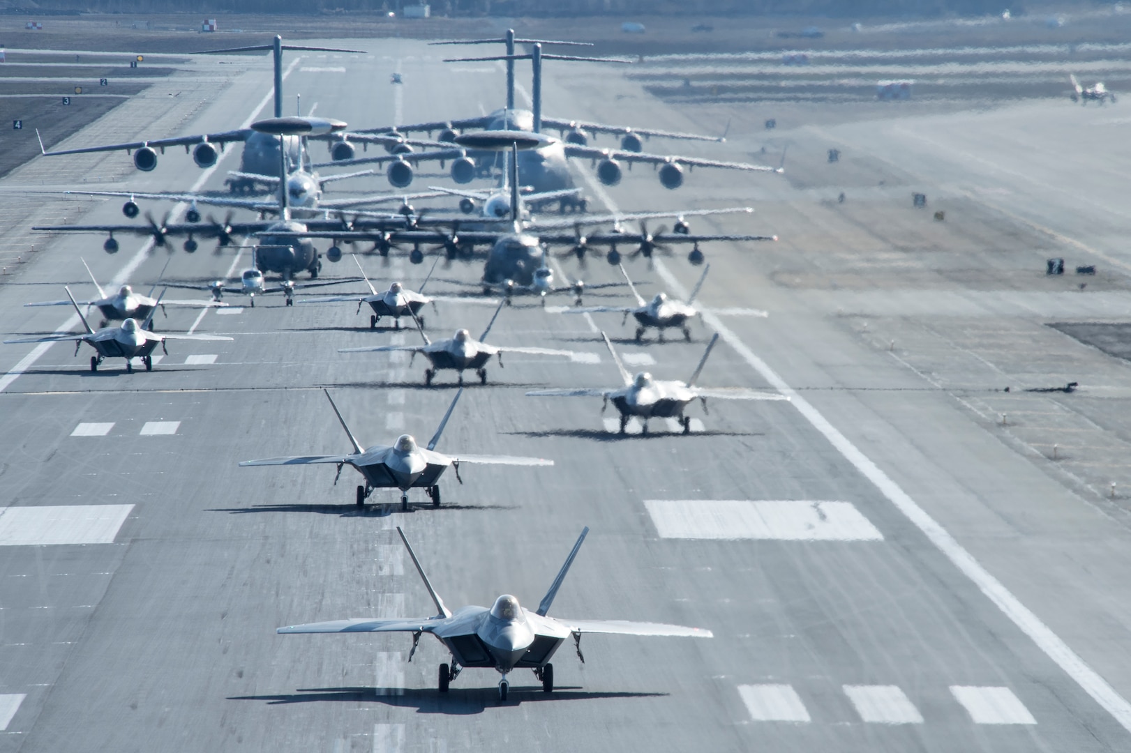 U.S. Air Force F-22 Raptors, E-3 Sentrys, C-17 Globemaster IIIs, C-130J Herculeses and C-12F Hurons participate in a close formation taxi known as an elephant walk at Joint Base Elmendorf-Richardson, Alaska, May 5, 2020. This event displayed the ability of the 3rd Wing, 176th Wing and the 477th Fighter Group to maintain constant readiness throughout COVID-19 by Total Force Integration between active-duty, Guard and Reserve units to continue defending the U.S. homeland and ensuring a free and open Indo-Pacific.