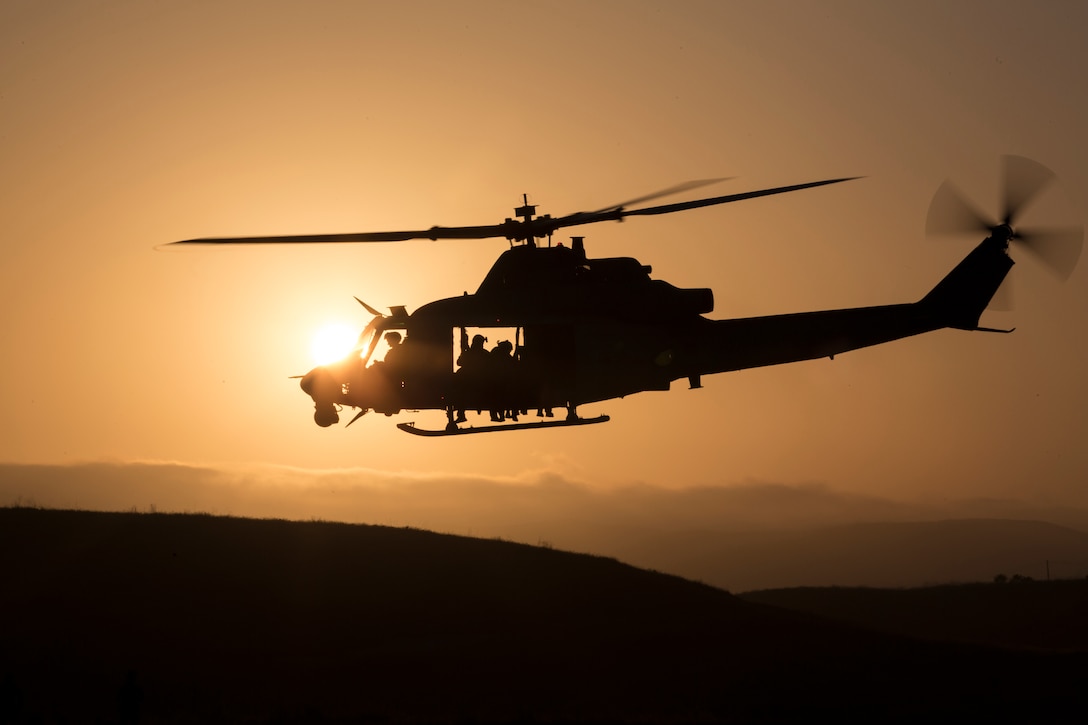 A silhouetted helicopter flies above hills.