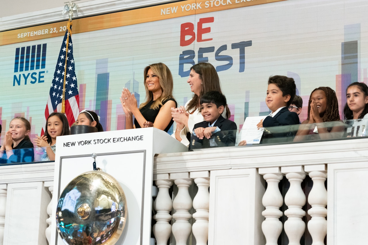 A woman, surrounded by children, claps from a balcony.