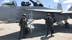 Two navy pilots pose near an aircraft.