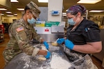 U.S. Army Spc. Kyla Bowman, left, culinary specialist, Foxtrot Company, 250th Brigade Support Battalion, New Jersey Army National Guard, prepares a Stromboli while Head Cook Casie Smickle observes at Veterans Haven North, Glen Gardner, N.J., April 30, 2020. Five New Jersey National Guard Soldiers and three Airmen are assisting the kitchen staff, which is responsible for preparing 2,400 meals a day for residents of the Haven and the Hunterdon Developmental Center.