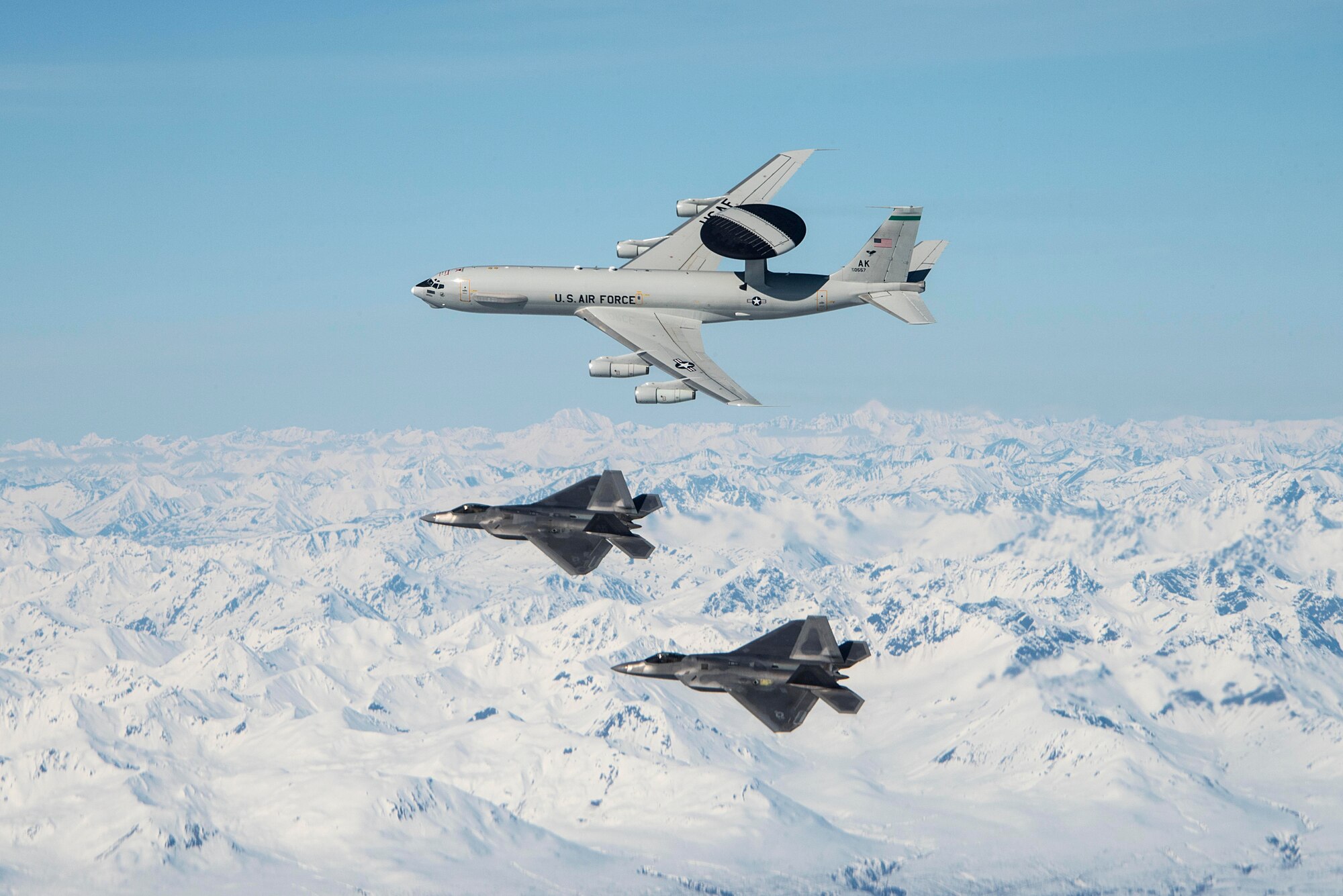 An E-3 Sentry and two F-22 Raptors assigned to Joint Base Elmendorf-Richardson (JBER) in Anchorage, Alaska fly over mountains in Alaska May 5, 2020.