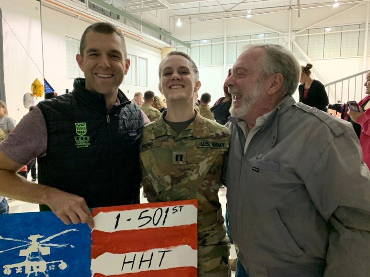 A soldier stands smiling with her father and grandfather on either side of her.