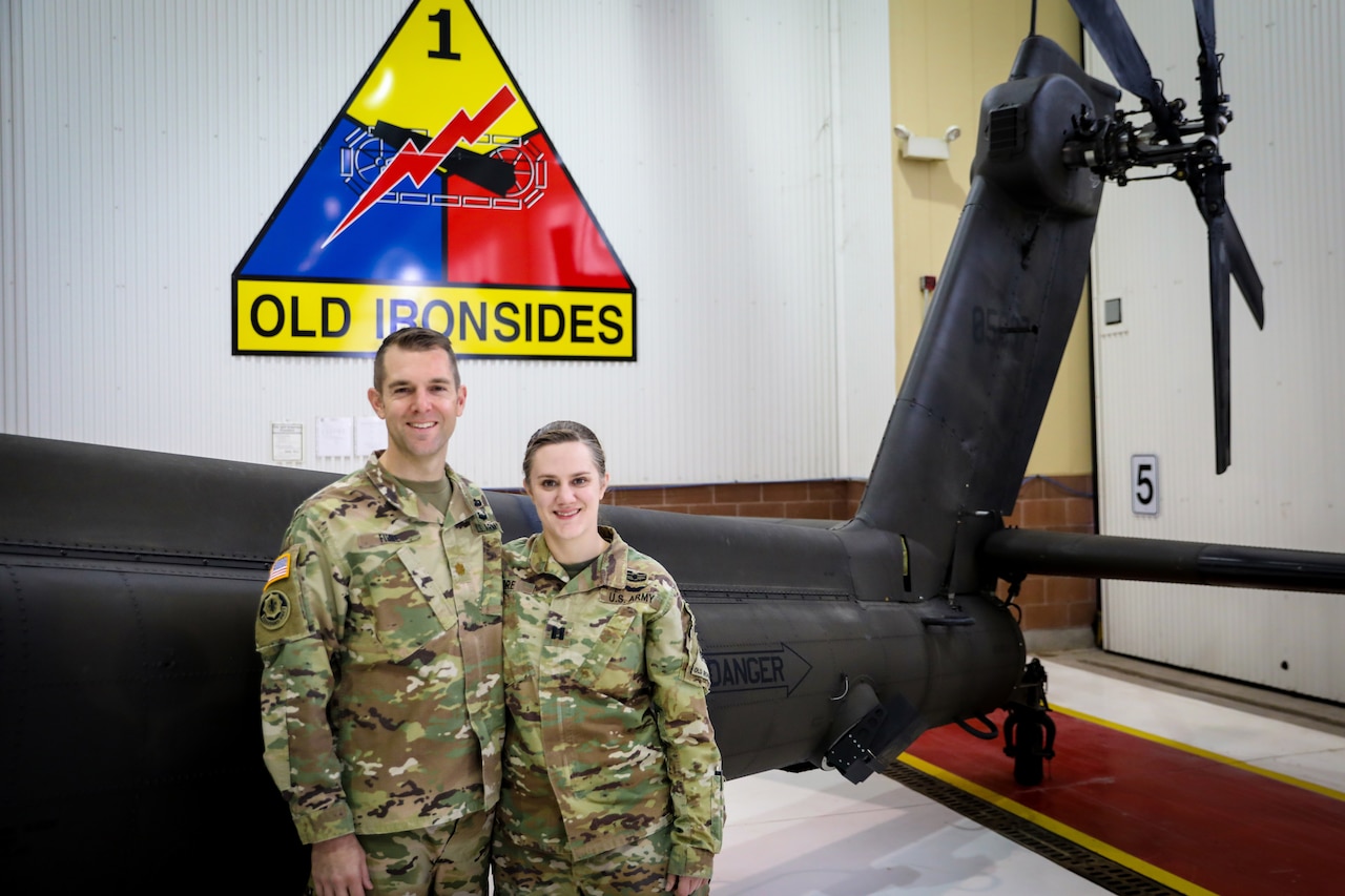 Two soldiers pose in front of the tail end of a helicopter.