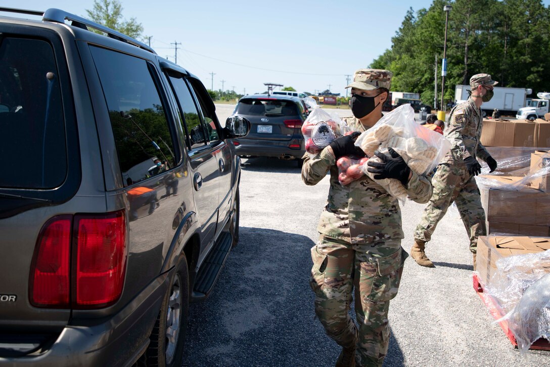 A soldier wearing a face mask and gloves carries bags of food.