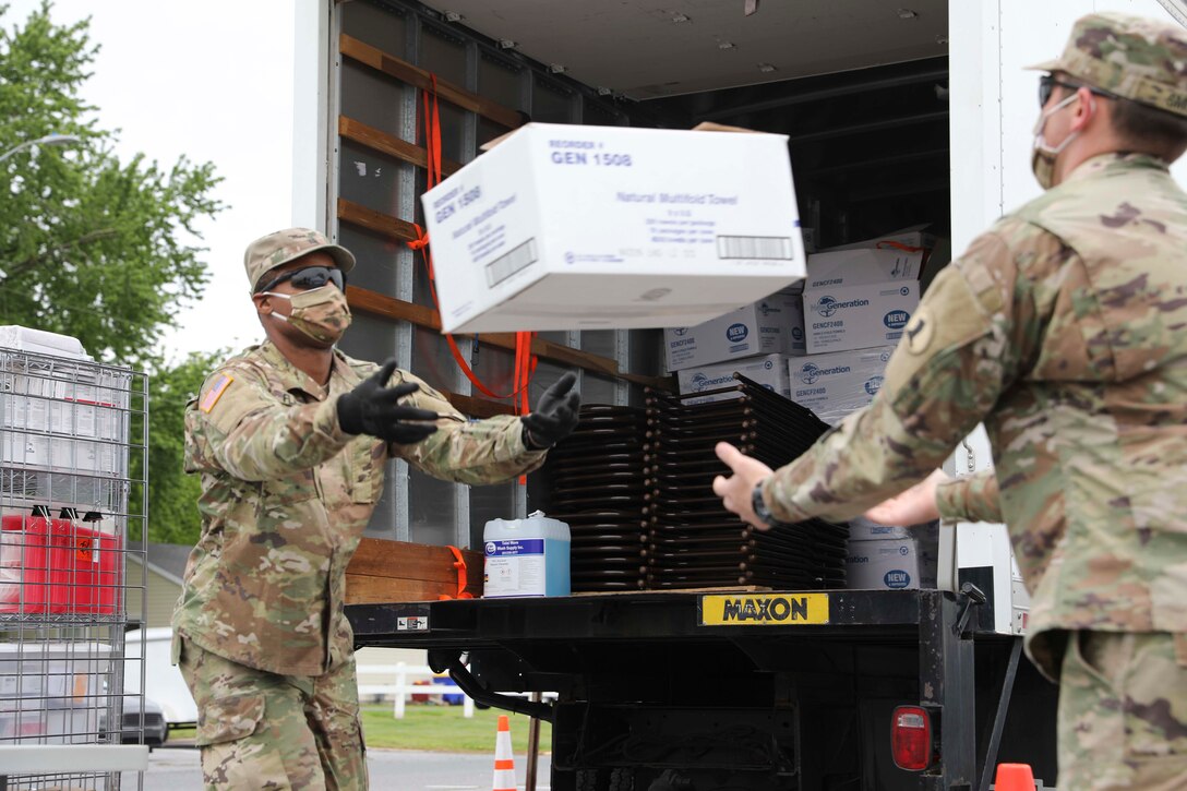 Two soldiers wearing face masks offload boxes from a truck.