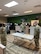 Three males in green camouflage uniforms and face masks stand around a table in a room with green and grey walls and grey chevron carpets.