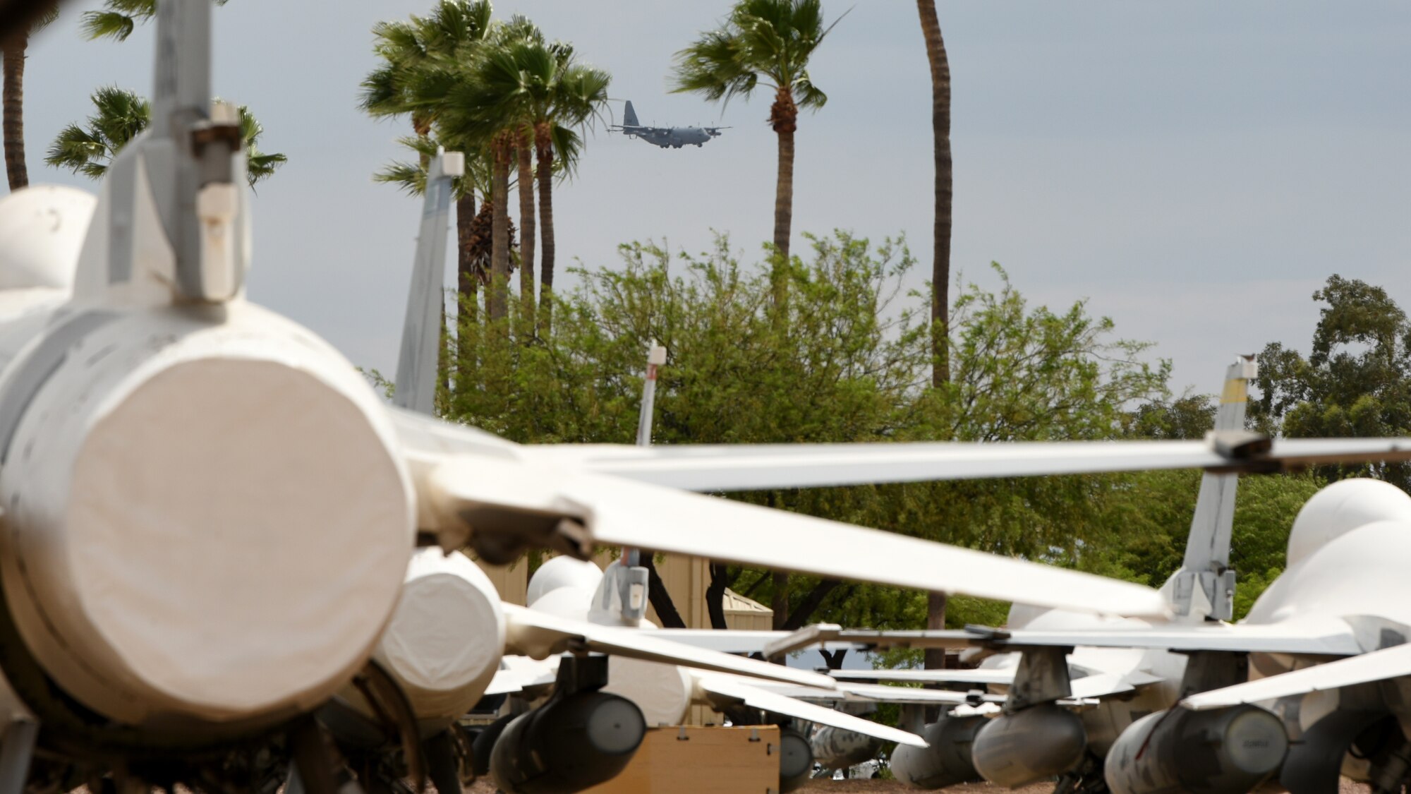 A photo of a C-130 Compass Call flying by various F-16 Fighting Falcons on the ground