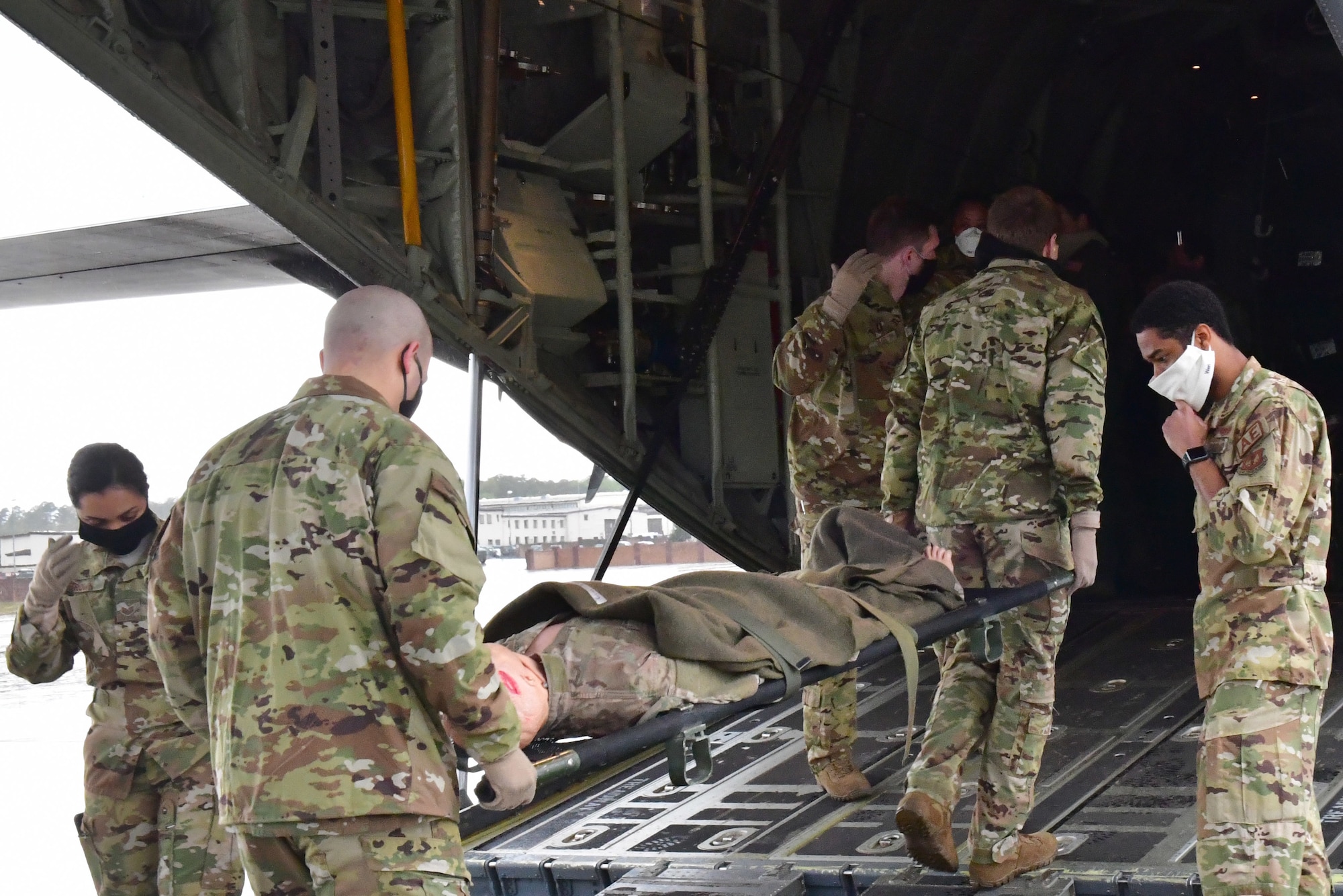 Airmen carry a mannequin on a gurney onto an aircraft.