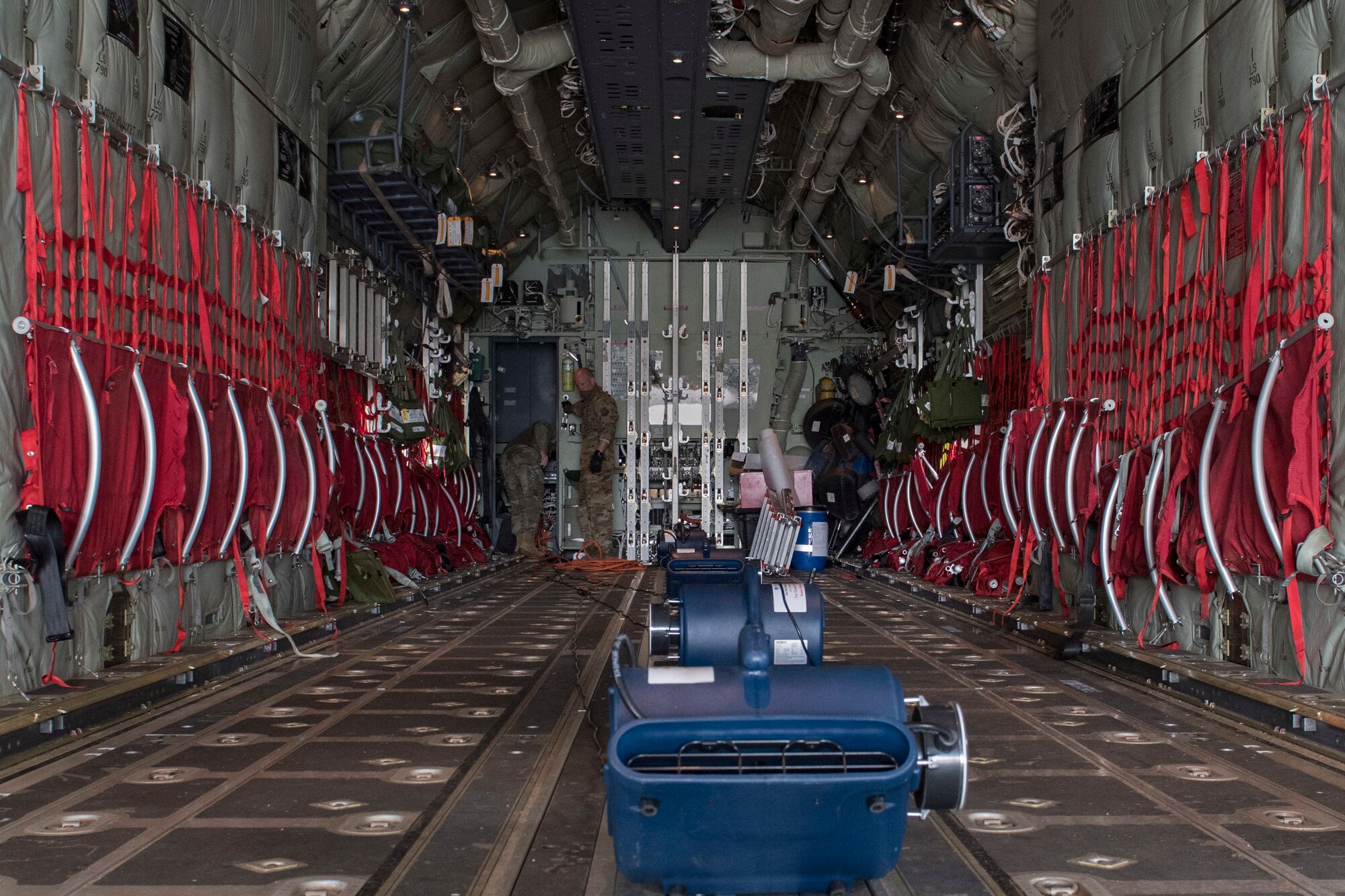Two Airmen stand inside an aircraft next to a row of ion distribution units.