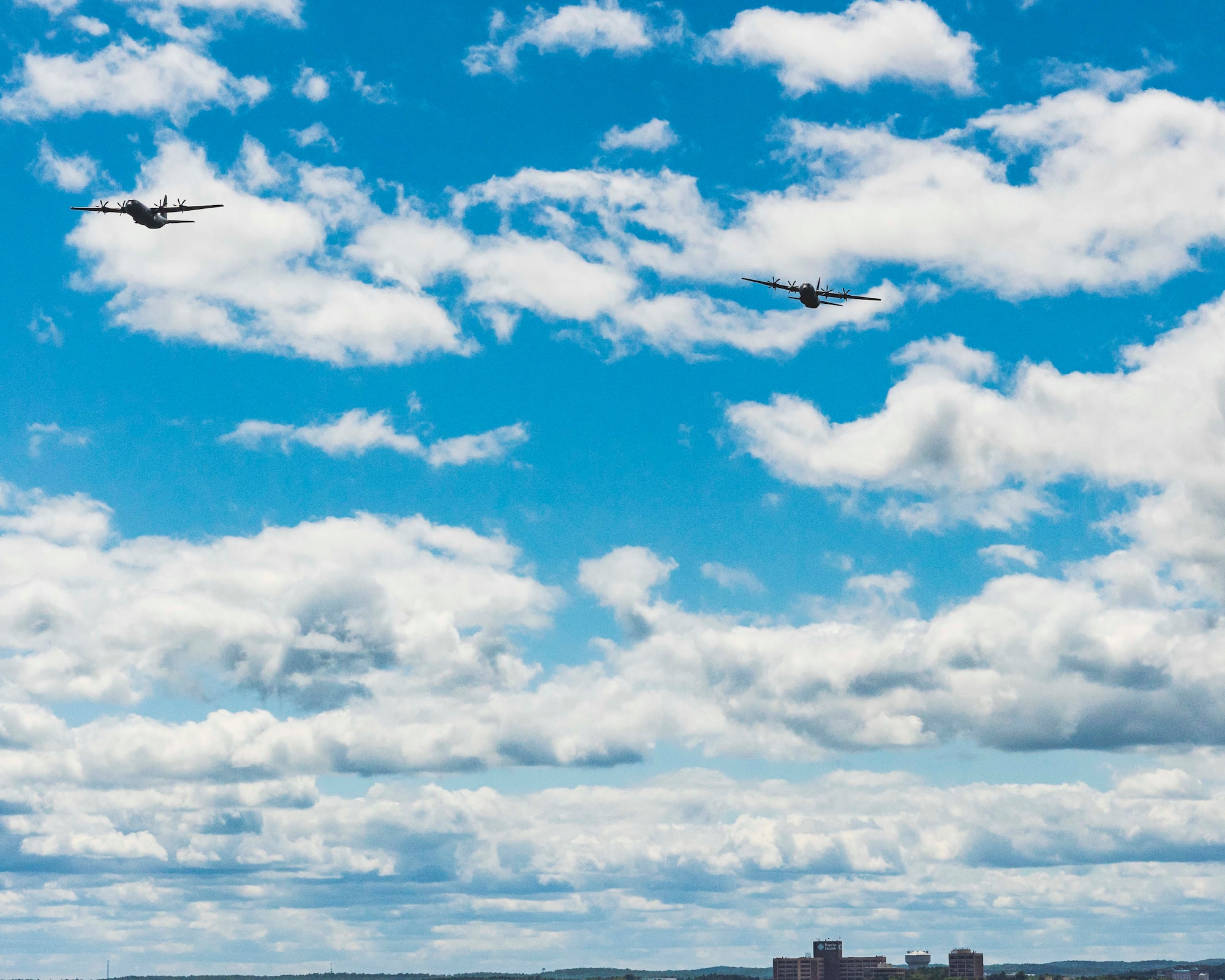 People watch as two C-130s fly over the city