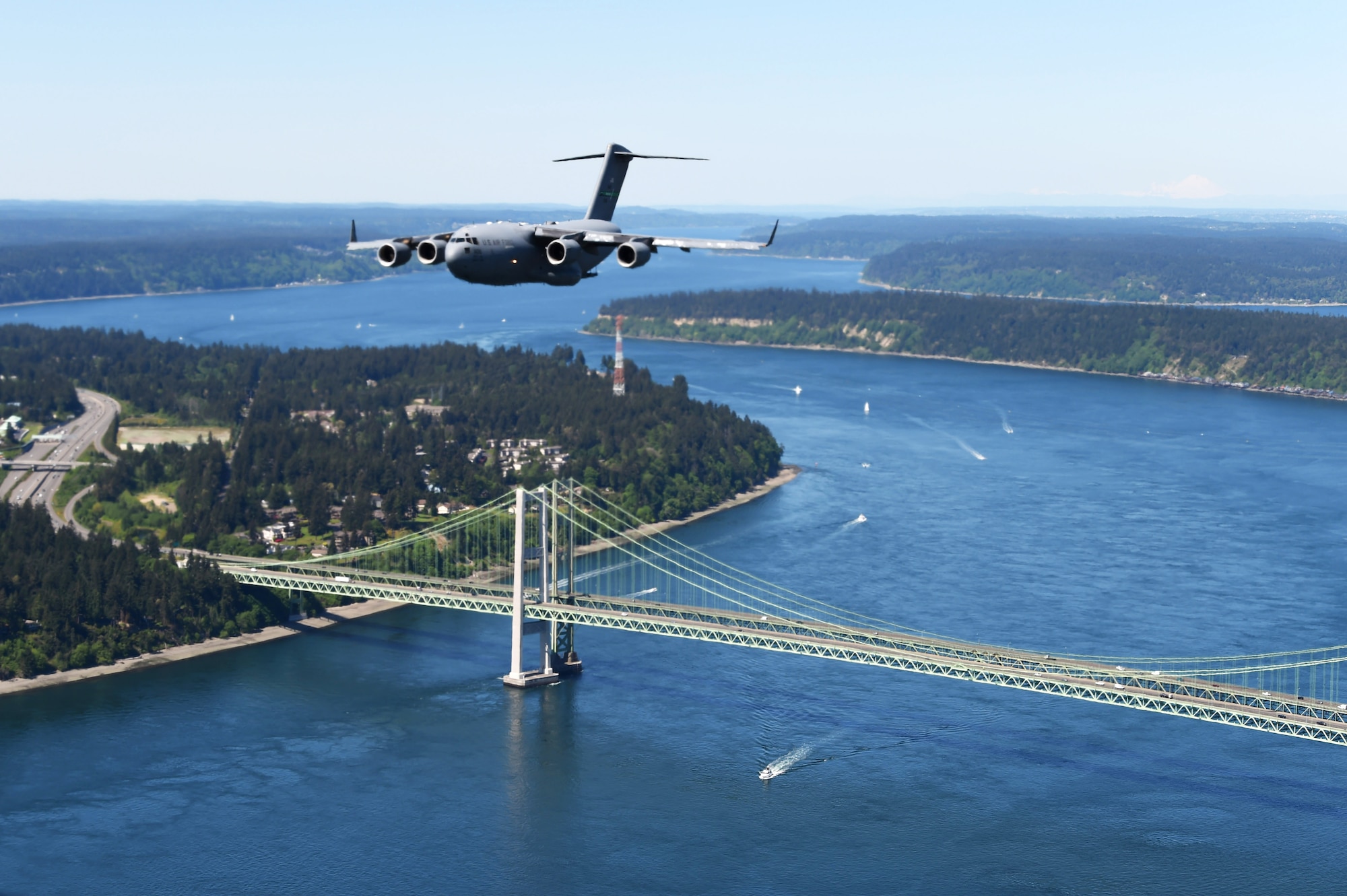 A C-17 Globemaster III from Joint Base Lewis-McChord, Wash., flies over the Tacoma Narrows Bridge in Tacoma, Wash., May 8, 2020. The 62nd Airlift Wing C-17 Demonstartion Team, made up of pilots and loadmasters from the 4th, 7th, and 8th Airlift Squadrons, conducted a flyover of nearly 45 hospitals, healthcare, organizations and landmarks up and down the Puget Sound, in appreciation of those working during the COVID-19 pandemic. (U.S. Air Force photo by Airman 1st Class Mikayla Heineck)