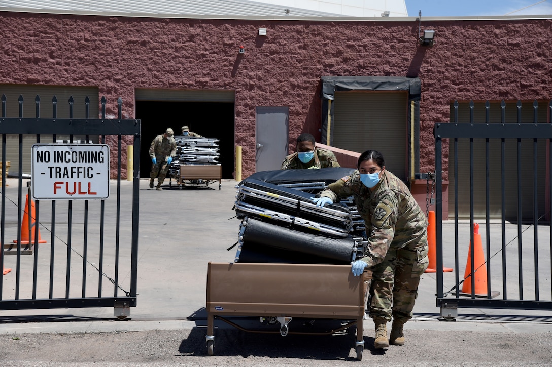 Service members wheel portable hospital beds out of a storage building.