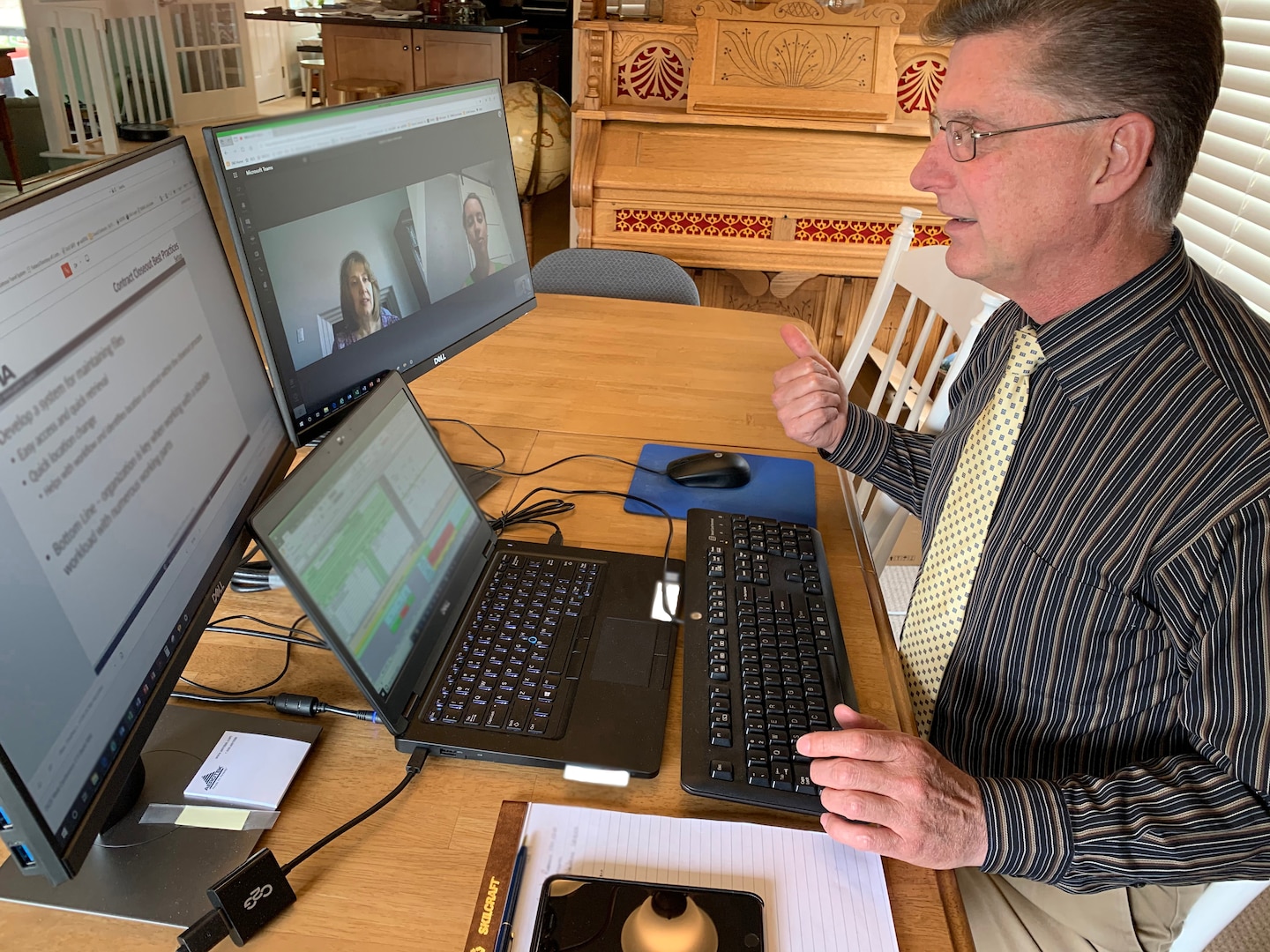 Man sits at his table while teaching training to two female colleagues who appear on his screen monitor