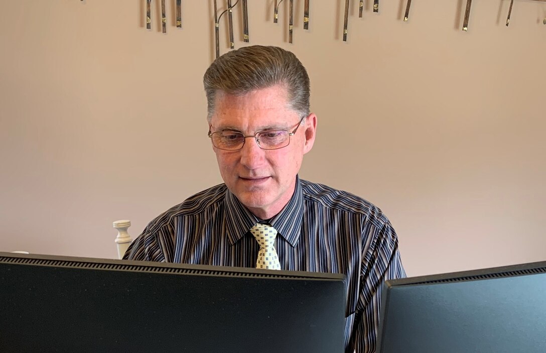 Man sits at his table wearing a dark stripped shirt while working on his computer