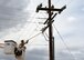 Photo of a electrical systems shop Airman stands in a truck manlift while performing emergency maintenance on an electric pole