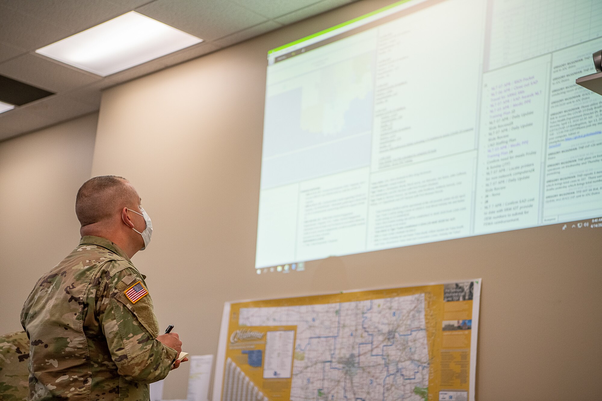 Oklahoma Army National Guard Lt. Jeremie Fisher, a chaplain assigned to the Oklahoma Joint Task Force from the 1st Battalion, 279th Infantry, 45th Infantry Brigade Combat Team, writes down overall Army and Air National Guard numbers and unit assignments from a projection while working within the Oklahoma Joint Task Force at the Multiagency Coordination Center in Oklahoma City, April 14, 2020. Oklahoma Gov. Kevin Stitt activated 175 additional Oklahoma Army and Air National Guardsmen, April 13, 2020, to aid various missions in support of the state’s response to COVID-19. (U.S. Air National Guard photo by Tech. Sgt. Kasey M. Phipps)