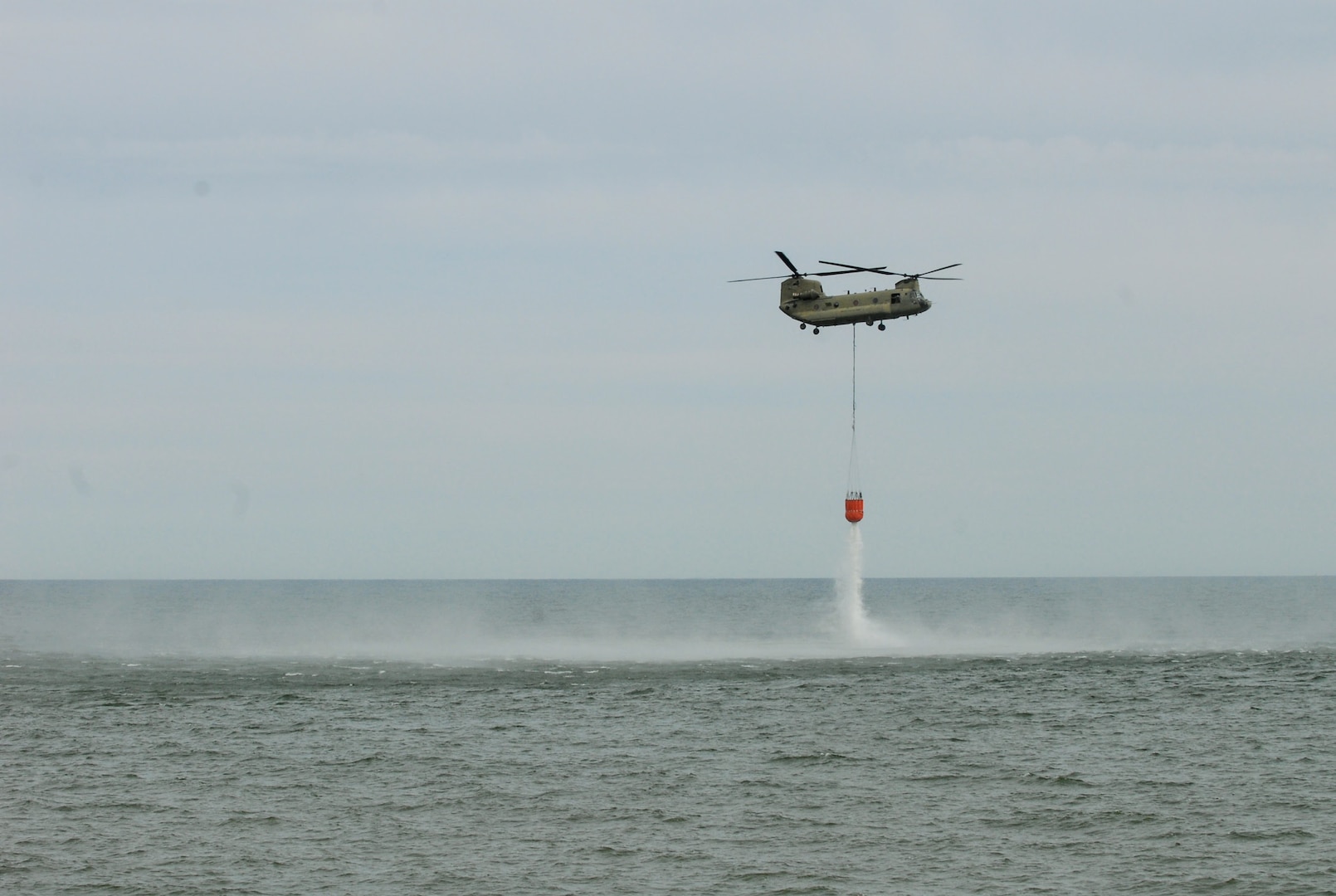 A New York Army National Guard CH-47 Chinook helicopter dumps 2,000 gallons of water from a bucket over Lake Ontario near Hamlin, New York, May 6, 2020. The Chinook's pilots and crew were practicing scooping and dumping water in preparation for firefighting missions.