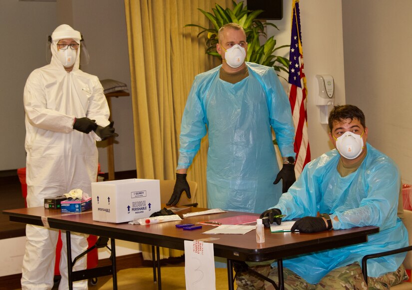 Three National Guard soldiers wearing protective equipment man a COVID-19 testing site.