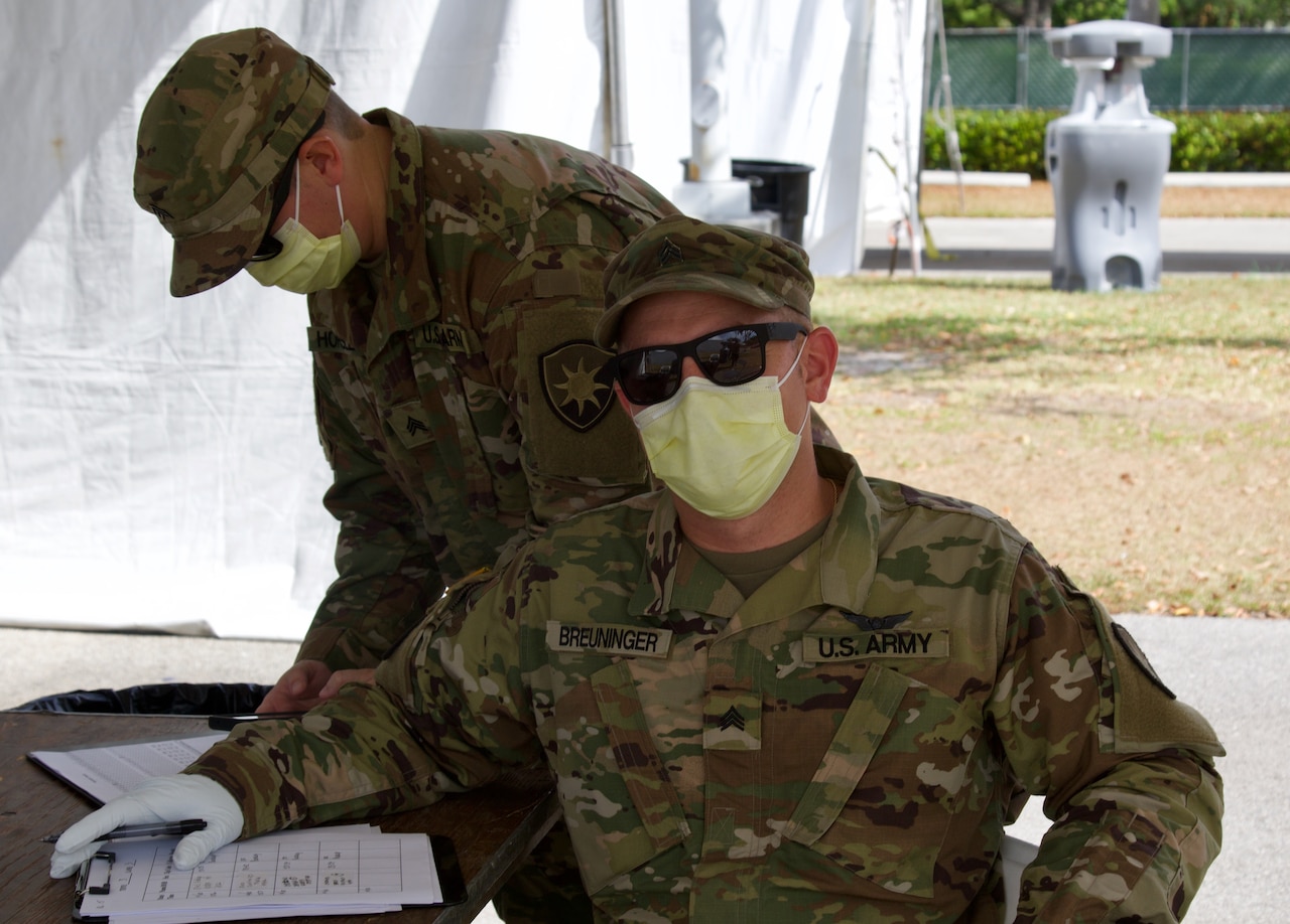 Two National Guard soldiers wearing masks work at a check-in site for COVID-19 testing.