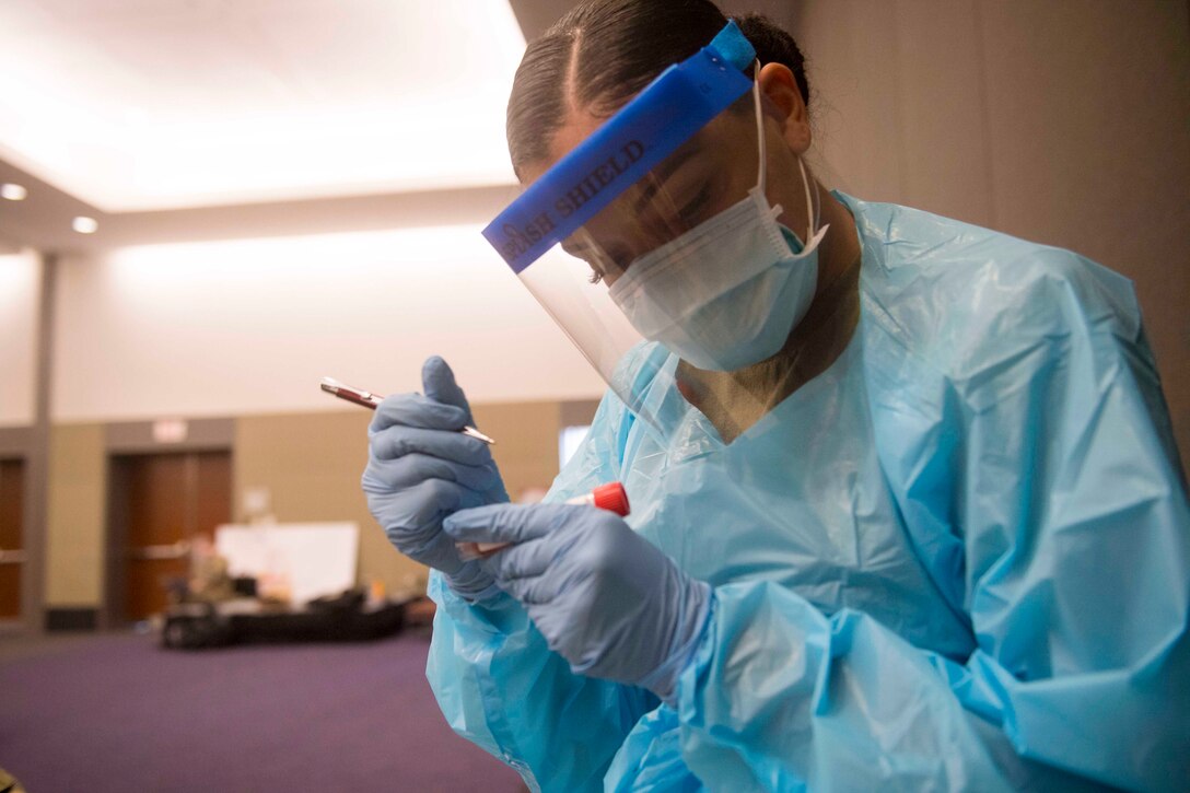 A soldier wearing personal protective equipment labels a test tube.