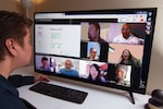 Man at a computer speaking to multiple colleagues through a virtual teleconference