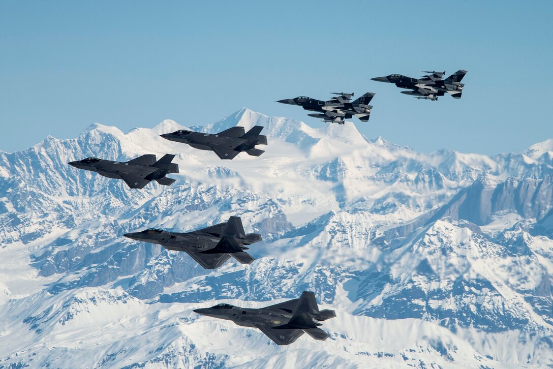 Six Air Force aircraft fly near snowy mountains.