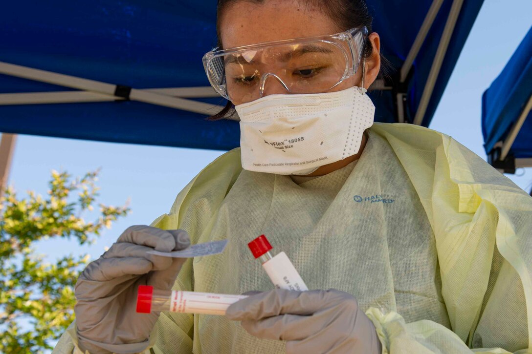 A medical technician wearing a mask and gloves labels a nasal swab.