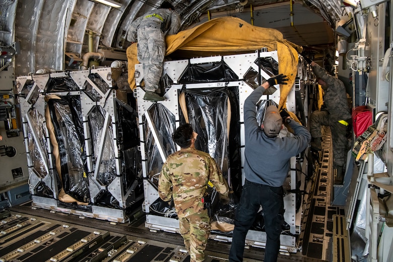 Airmen cover two Transport Isolation Systems with tarps due to inclement weather at Dover Air Force Base, Delaware, April 30, 2020. The TIS units were delivered to Dover AFB by C-17 Globemaster III from Joint Base Charleston, South Carolina. In accordance with health protection policies, Dover AFB will serve as the sole hub for TIS decontamination on the East Coast. (U.S. Air Force photo by Senior Airman Christopher Quail)
