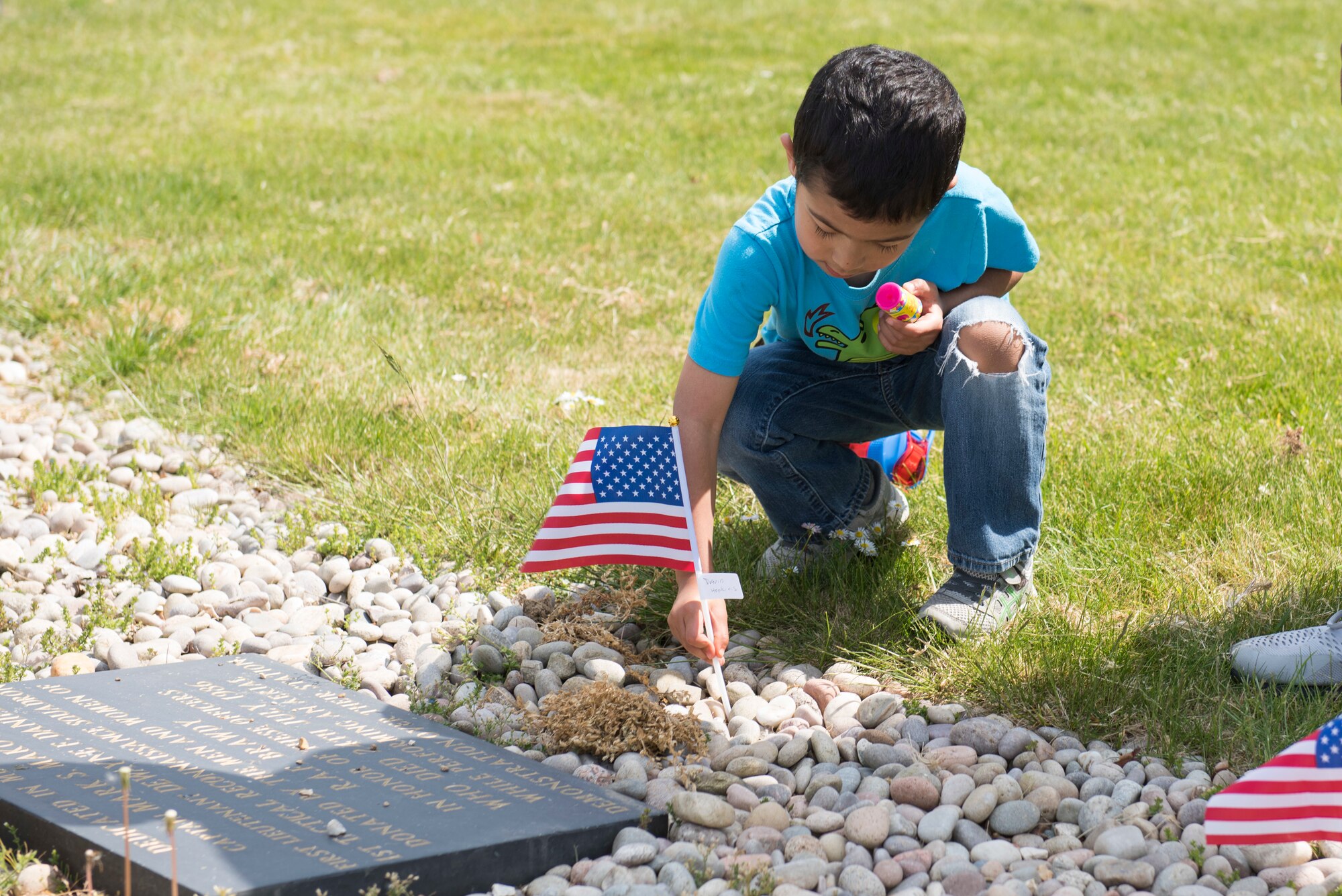 David Hopkins places a U.S. flag at a World War II memorial during the Victory in Europe Day Scavenger Hunt at RAF Alconbury, England May 8, 2020. While keeping with COVID-19 physical distancing guidelines, the self-guided walking tour on base was geared toward teaching children and families the events that led to the end of World War II as they exercised. (U.S. Air Force photo by Airman 1st Class Jennifer Zima)