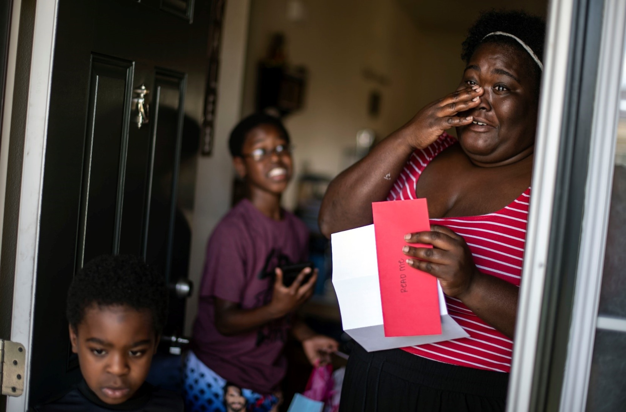 A woman stands in the doorway of her home with her two grade school-aged sons while she holds an envelope holding a letter from her deployed husband.