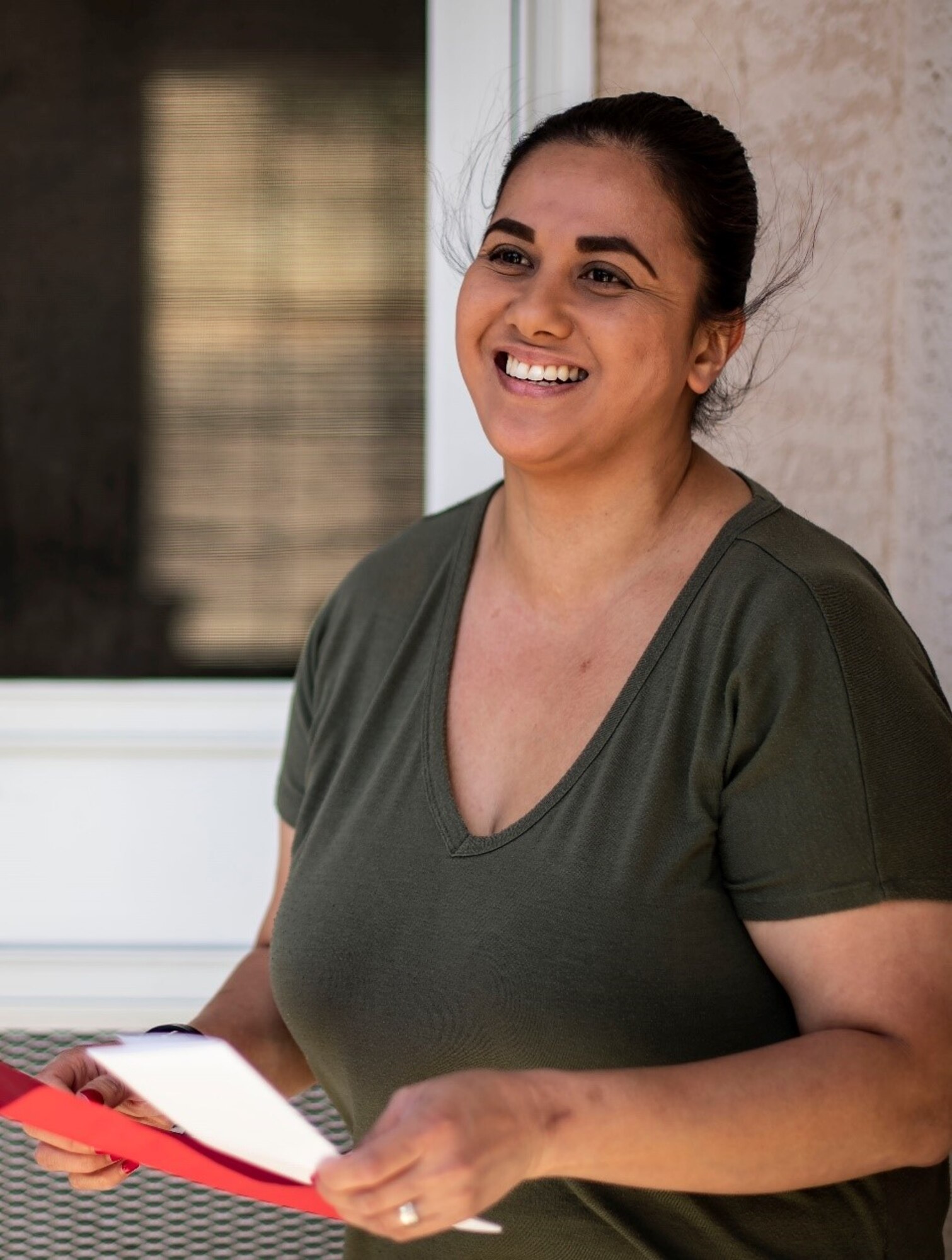 A smiling woman stands in the doorway of her home and holds an envelope holding a letter from her deployed husband.