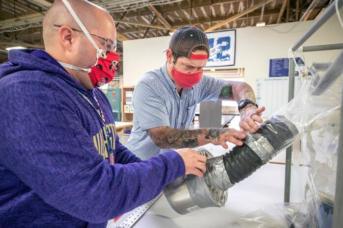 John A. Carver, left, and Michael Dennis, supervisors with Shop 64 Sail Loft, install a HEPA filter on a new biocontainment system prototype for use on Navy vessels May 4, 2020 inside the Building 460, at Puget Sound Naval Shipyard & Intermediate Maintenance Facility in Bremerton, Washington.