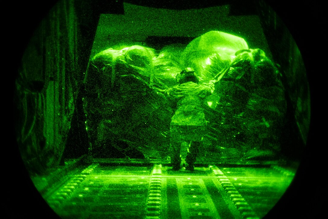 An airman, illuminated in green light by a night-vision lens, guides cargo onto an aircraft.