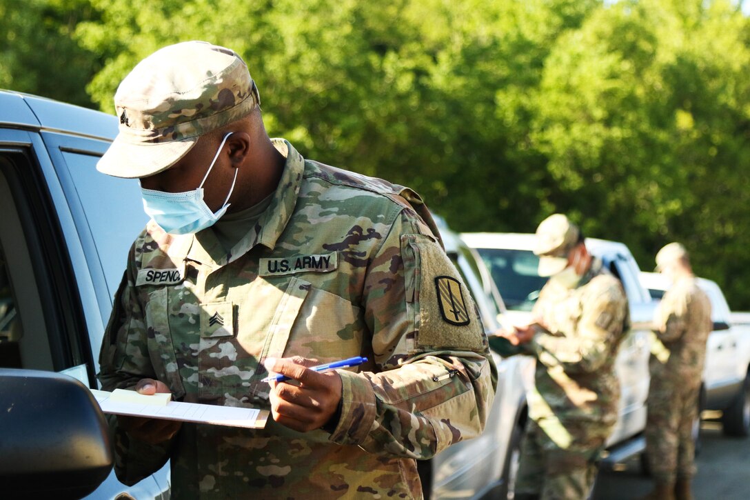 Three soldiers holding clipboards and pens talk to people inside a line of vehicles.