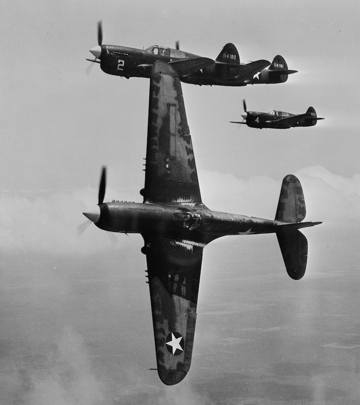 Three P-40F planes flying with one of them flying on its side showing the wings vertical.