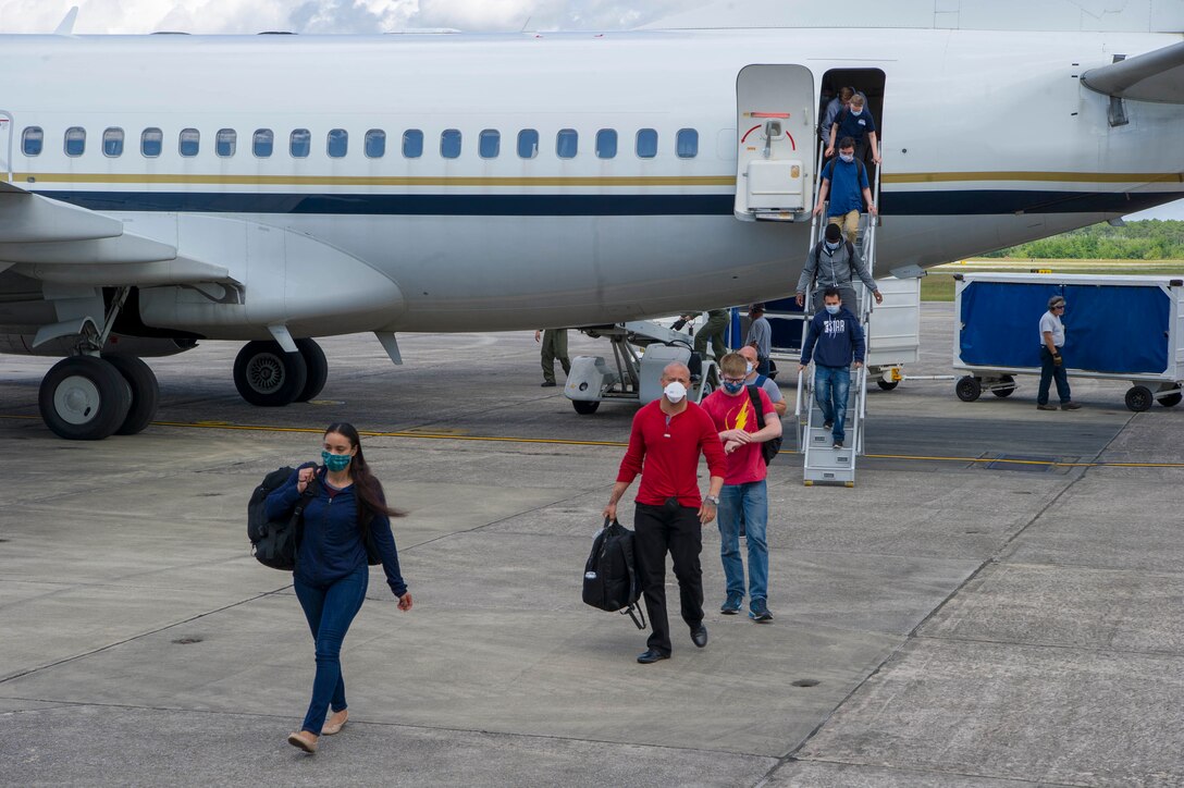 Sailors wearing civilian clothes and face masks exit from an airplane.
