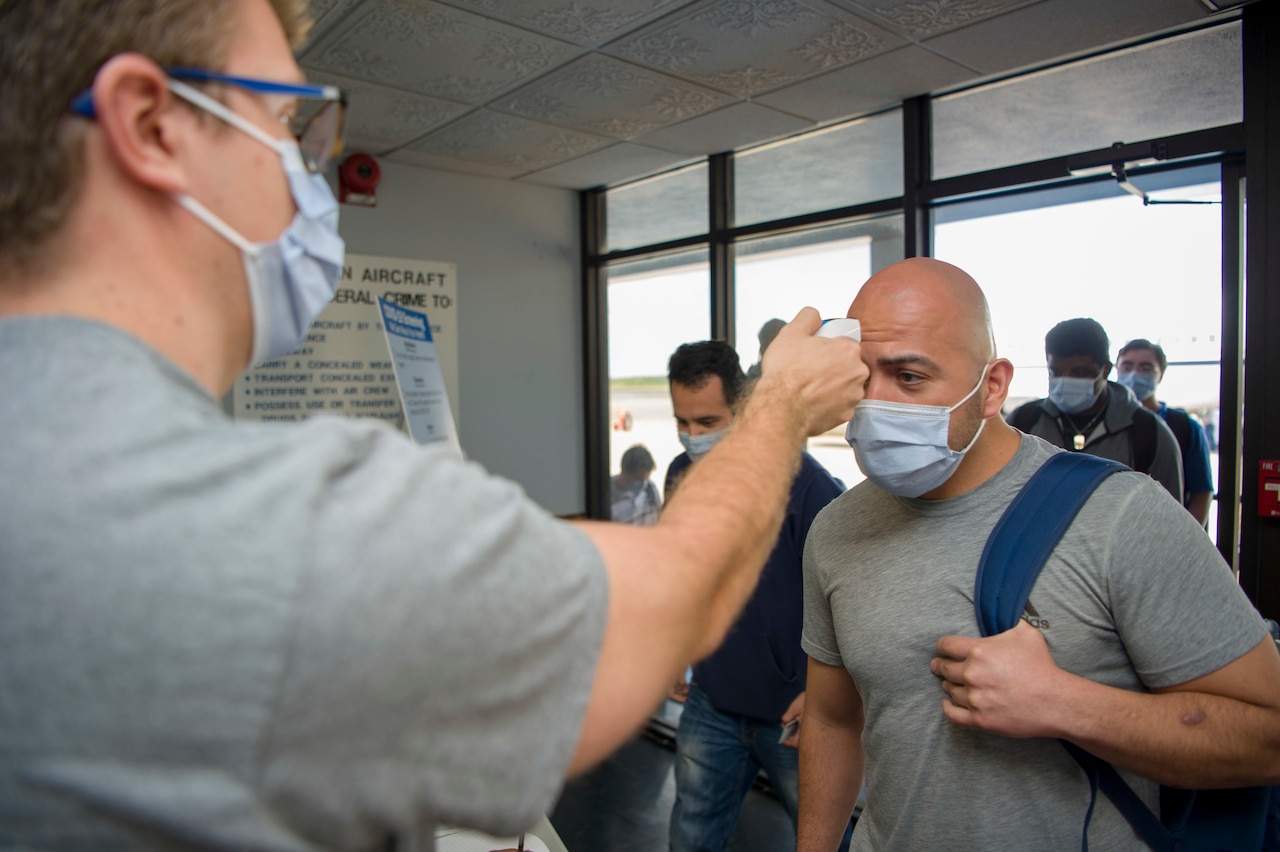 A man uses a forehead scanner to take another man’s temperature.