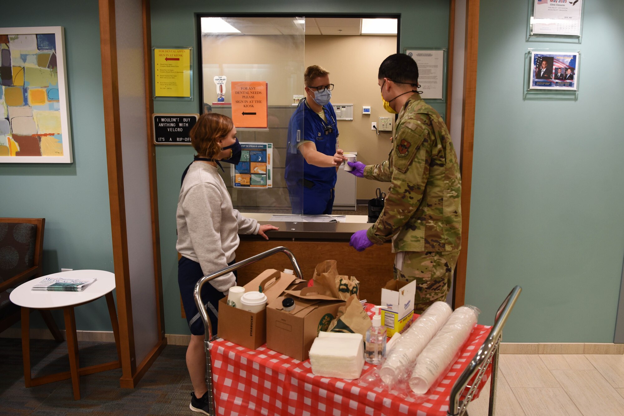 Staff Sgt. George Mills (right), 14th Operational Medical Readiness Squadron Public Health Flight non-commissioned officer in-charge, and Senior Airman Tiebout (left), Medics Morale Council Vice president, hand a 14th Medical Group dental clinic worker a coffee May 8, 2020, inside the Kortiz Clnic on Columbus Air Force Base, Miss. The 14th Blaze Medics Morale Council came up with an idea called the `morale walk’ in which volunteers go around the entire medical center to pass around treats to the workers and spread positivity. (U.S. Air Force photo by Airman 1st Class Jake Jacobsen)