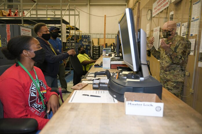 Photo shows personnel sitting on one side of plexiglass with supplies behind them and Bunch standing on the other side speaking to them through the plexiglass.