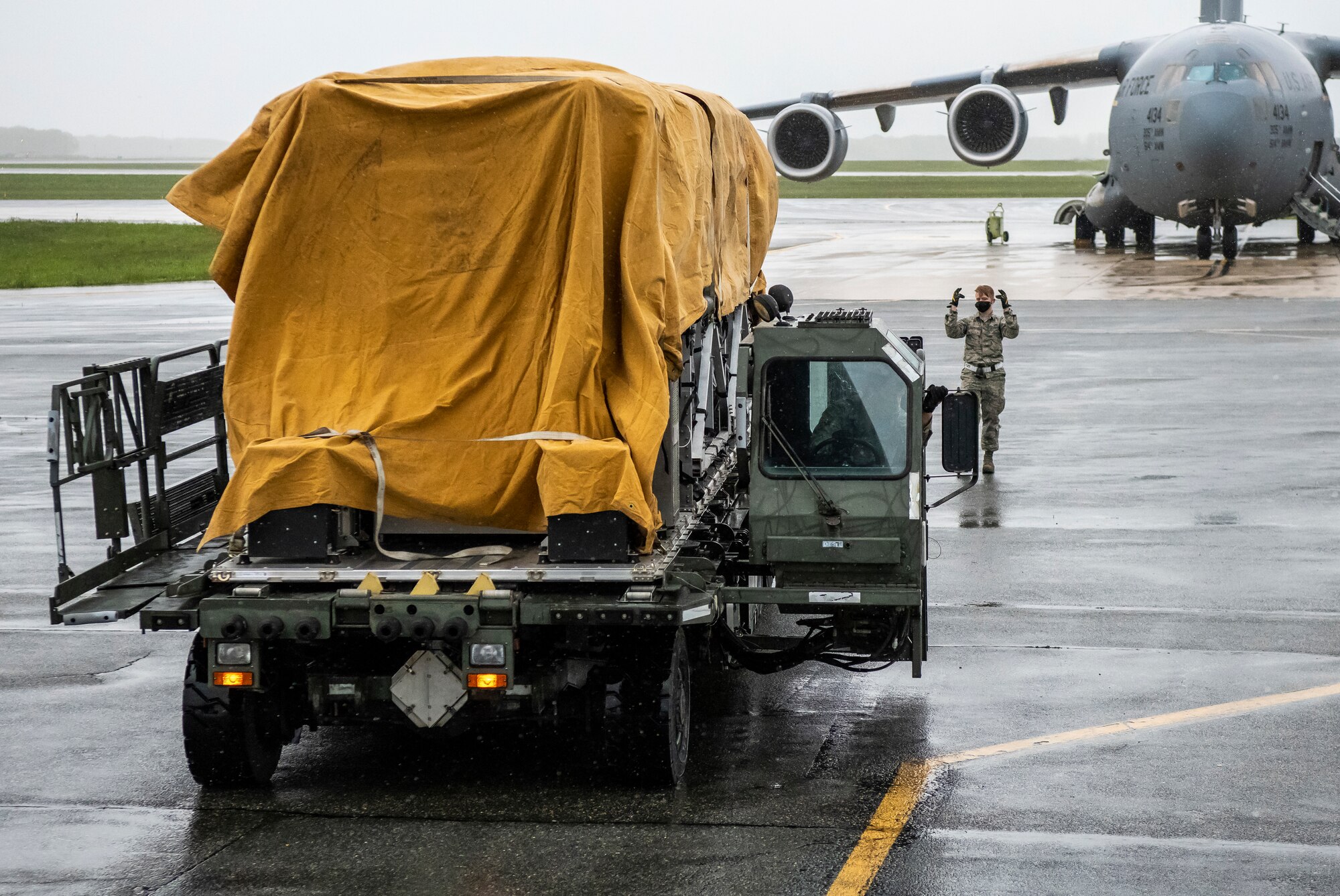 A 436th Aerial Port Squadron Airman guides a K-loader at Dover Air Force Base, Delaware, April 30, 2020. Tarps were placed on top of Transport Isolation Systems due to inclement weather at Dover AFB. In accordance with health protection policies, Dover AFB will serve as the sole hub for TIS decontamination on the East Coast. (U.S. Air Force photo by Senior Airman Christopher Quail)